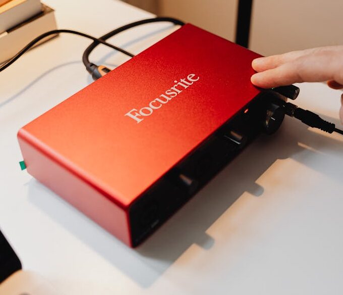 Detailed view of a red audio interface being operated by a hand on a desk.
